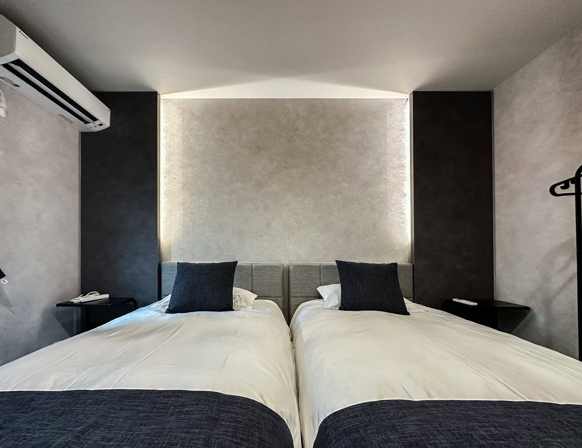 A hotel room with two beds, a large window, and a wall-mounted air conditioner.