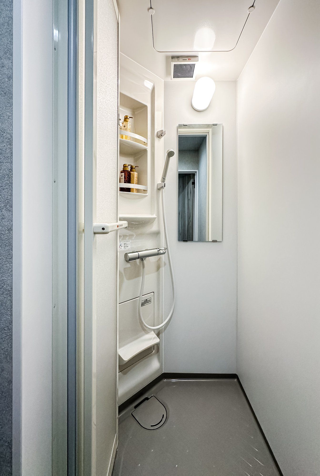 A compact bathroom with a shower, a toilet, and a small shelf with toiletries.