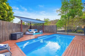 A swimming pool with a wooden deck, a covered seating area, and a wooden fence. - The Blue House Spacious Home (Port Macquarie)