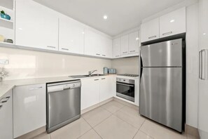 A modern kitchen with white cabinets, stainless steel appliances, and a tiled floor. - 16B Ocean front Apartment in the Peninsula (Surfers Paradise)