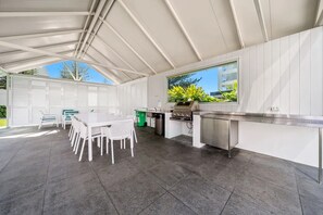 A covered outdoor kitchen area with a dining table and chairs, a grill, and a window overlooking greenery. - 16B Ocean front Apartment in the Peninsula (Surfers Paradise)