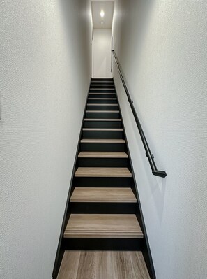 Eine moderne Treppe mit Holzstufen und einem Metallgeländer, die zu einer Zwischenebene mit Lichtschalter führt.