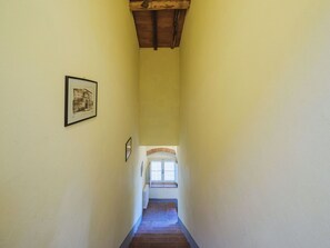 Ein schmaler Flur mit Holzboden, einem gerahmten Bild auf der linken Seite und einem Fenster am Ende.