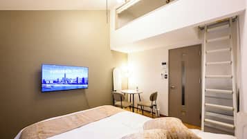 A hotel room with a bed, a television displaying a cityscape, a small table with chairs, and a door with a towel rack.