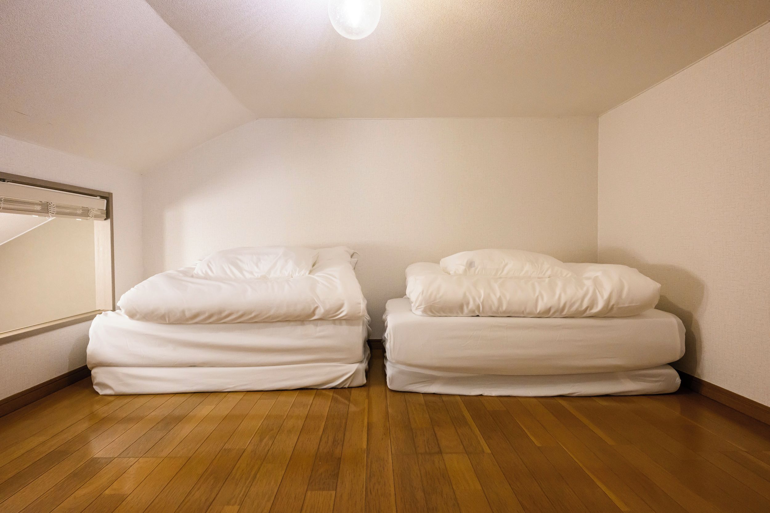 A room with two beds, wooden flooring, and a ceiling light fixture.