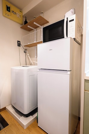 A compact kitchen with a white refrigerator, a microwave, and a washing machine. - Haku Loft Hakata 202 (Fukuoka)