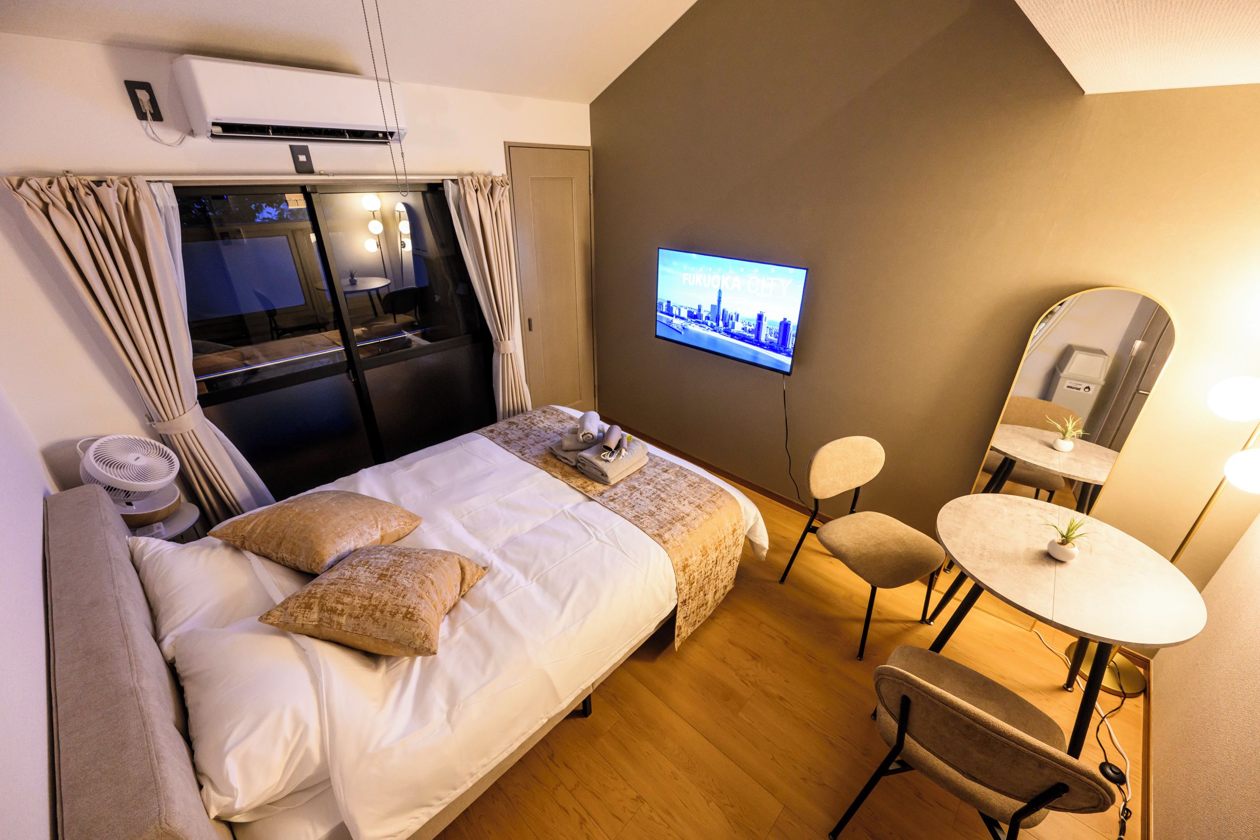 Ein Hotelzimmer mit einem Bett, einem Fernseher, einem Schreibtisch mit Stuhl und einem kleinen Tisch mit Pflanze.