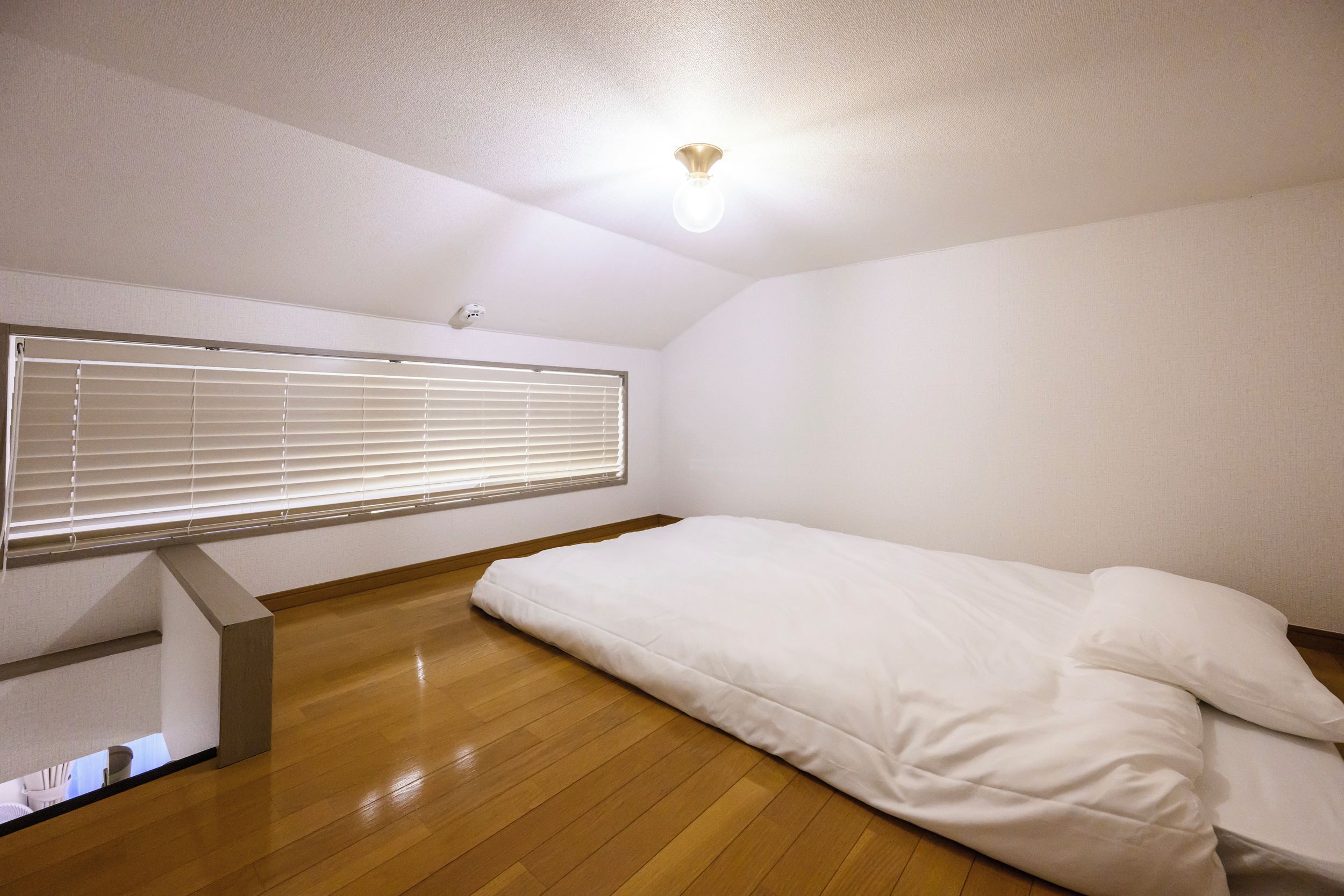 A room with a bed, a ceiling fan, and a window with blinds.