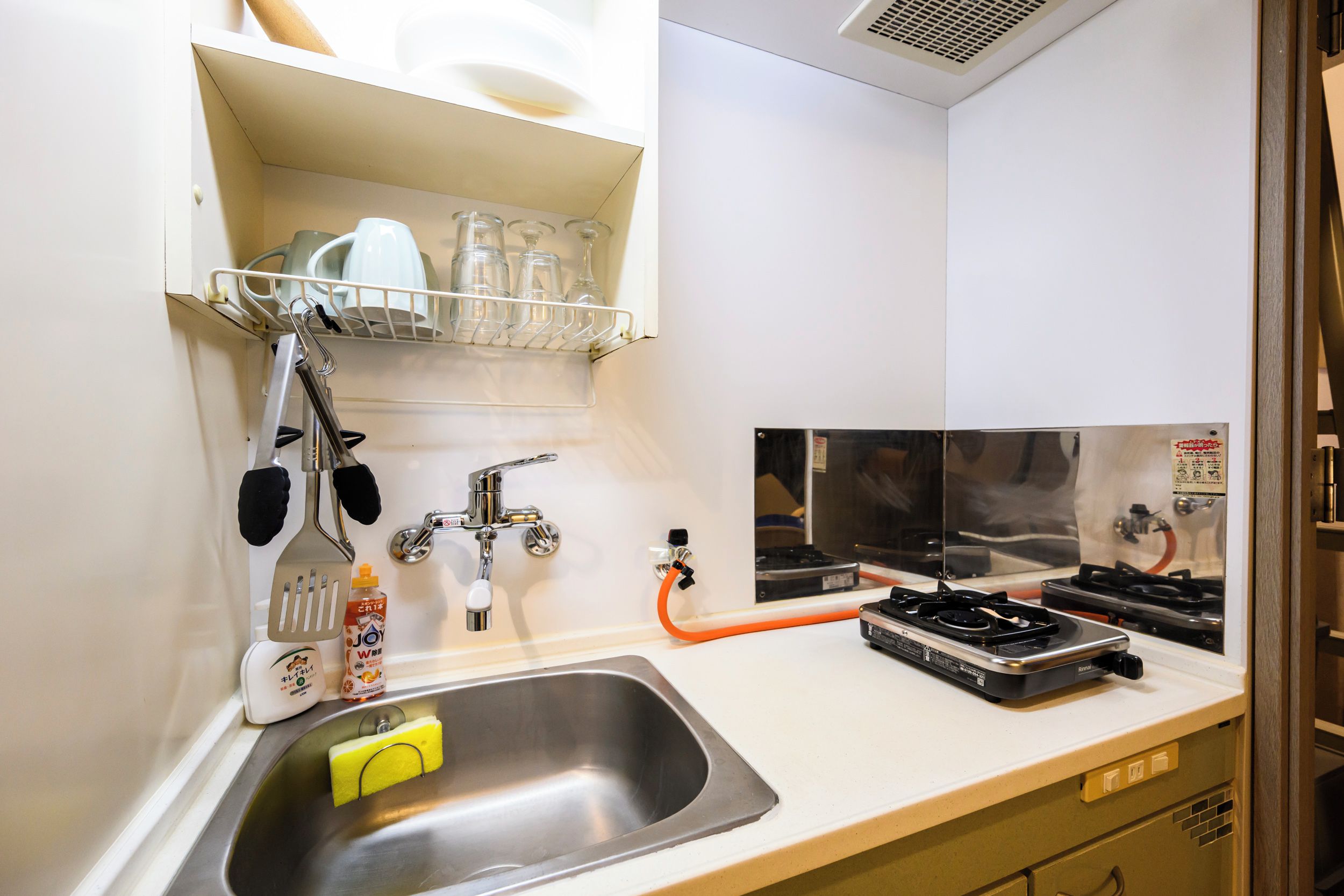 A kitchen with a stainless steel sink, a dish rack, a stove, and a faucet.