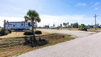 A gravel parking area with a white RV and a palm tree.