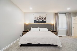 Una camera da letto con un letto, due comodini, una lampada a parete, una finestra con tende e una porta.