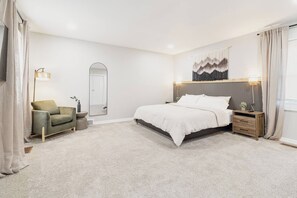 Una camera da letto con un letto, un comodino, una sedia, uno specchio e un quadro appeso al muro.