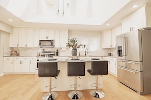 A modern kitchen with white cabinets, a stainless steel refrigerator, and a central island with bar stools. - Spacious Meridian Hills Retreat | Quiet & Private (Meridian Hills)