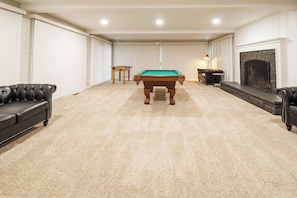 A room with a pool table, two leather sofas, a fireplace, and a carpeted floor. - Spacious Meridian Hills Retreat | Quiet & Private (Meridian Hills)