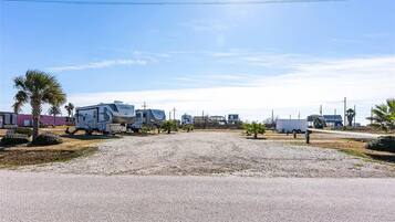 A gravel parking area with RVs and trailers, a clear sky, and sparse vegetation.