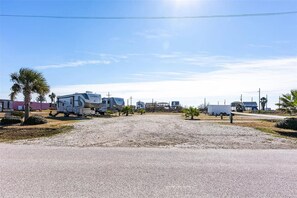 A gravel parking area with RVs and trailers, a clear sky, and sparse vegetation.