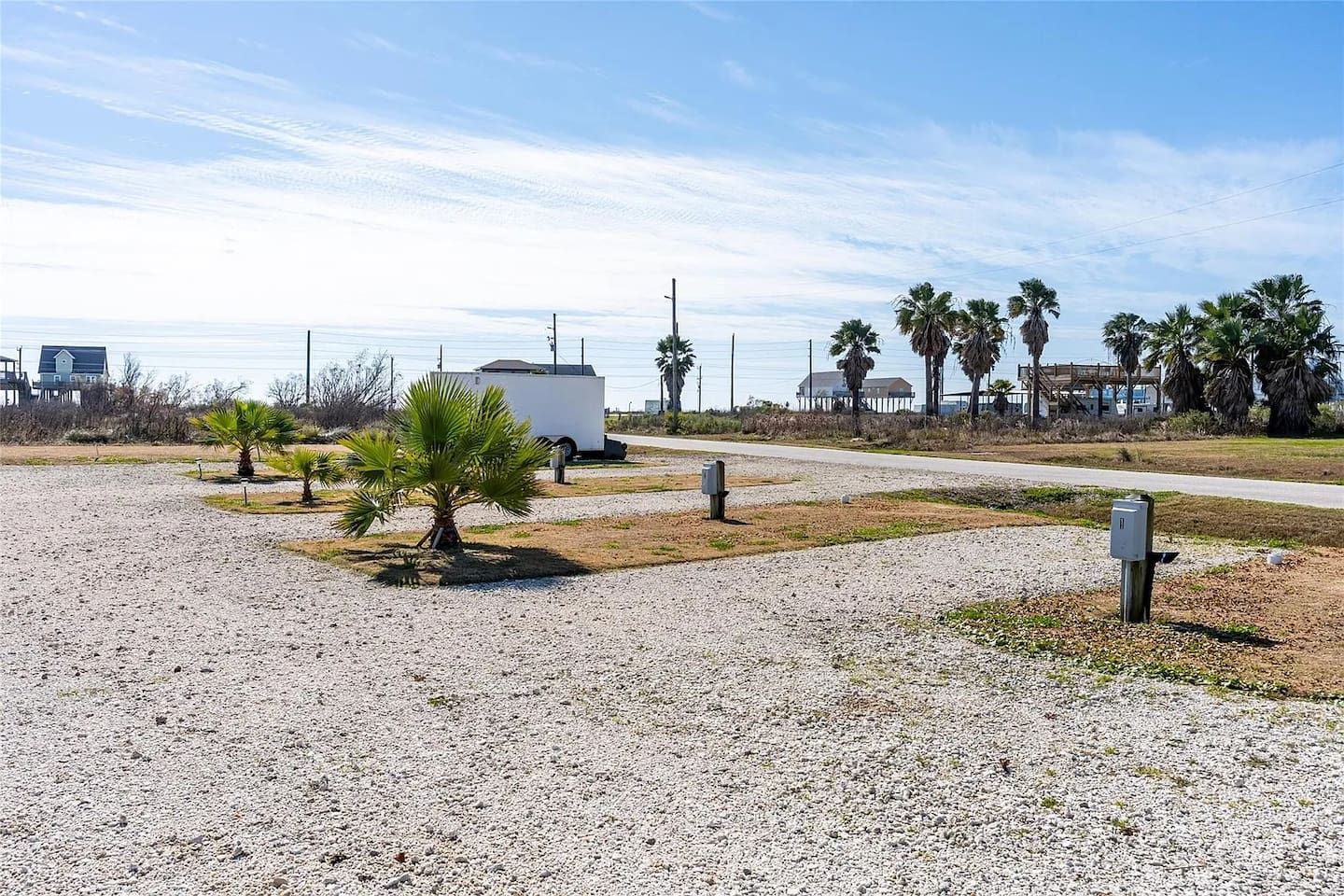 Ein Kiesparkplatz mit einer kleinen Palme, einem weißen Anhänger und einer Straße im Hintergrund.