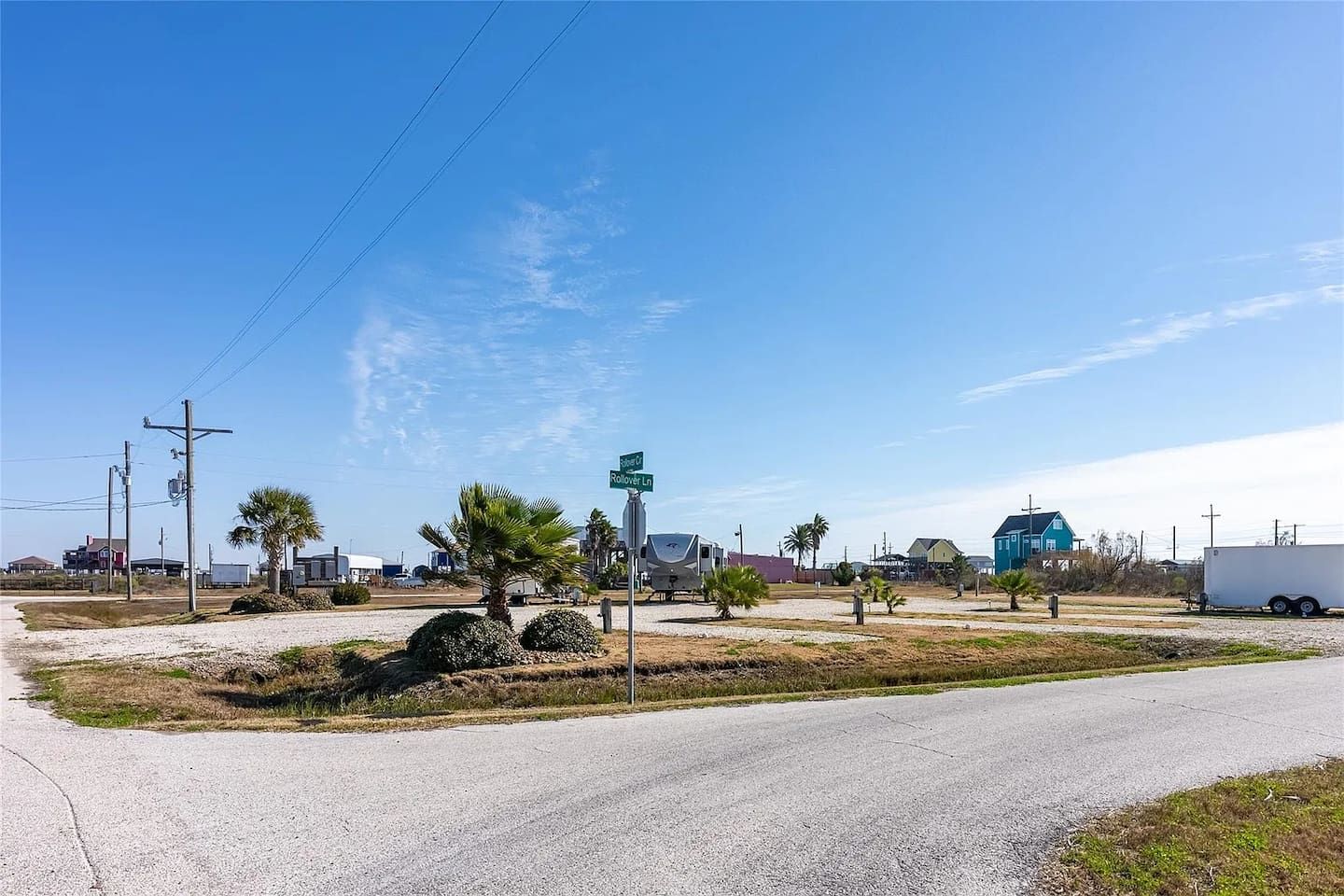 A road intersection with a green street sign, a gravel area with small bushes, and a clear blue sky.