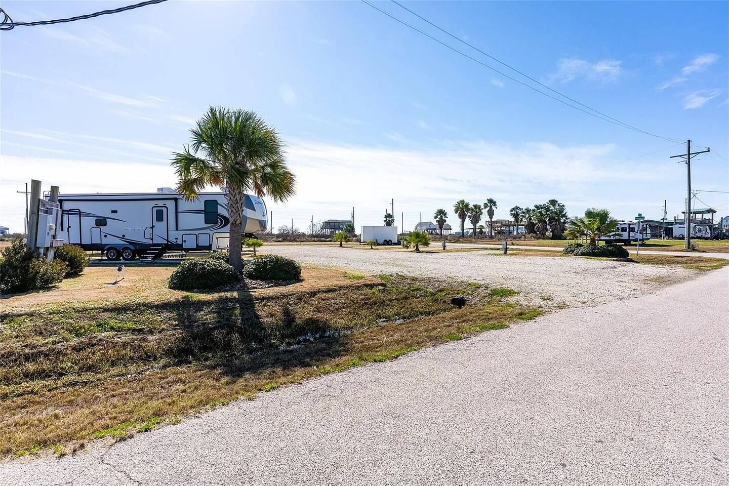 A gravel parking area with a white RV and a palm tree.