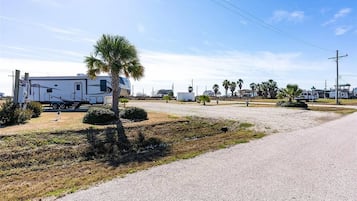 A gravel parking area with a white RV and a palm tree.