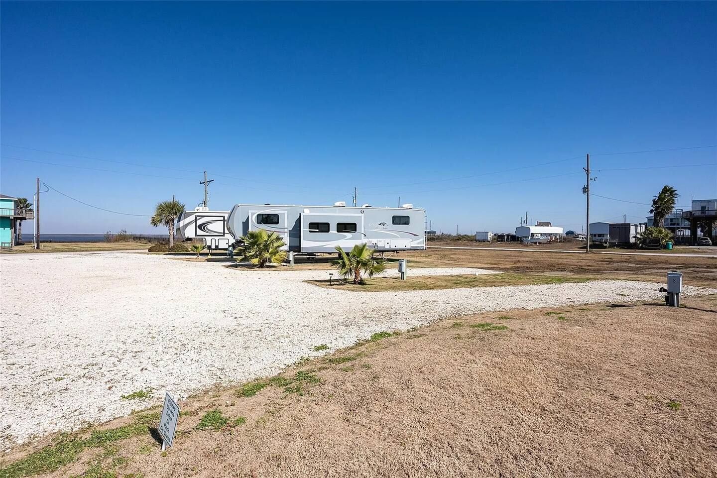 A campground with RVs parked on gravel, a clear sky, and a few palm trees.