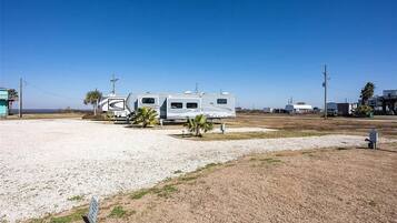 A campground with RVs parked on gravel, a clear sky, and a few palm trees.