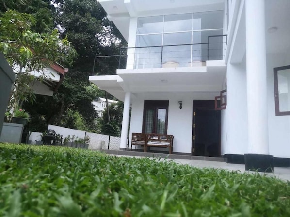 A modern two-story building with a balcony, a bench outside, and a well-maintained lawn. - Ivory Crest Villa (Kandy)