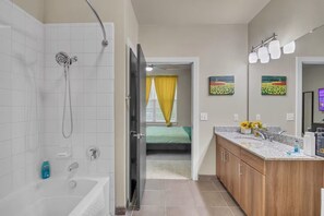 Een moderne badkamer met een douche, een bad en een toilet. Een bed is zichtbaar door een open deur in de aangrenzende kamer.