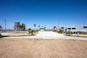Een RV-park aan het strand met een heldere lucht, een gebouw met balkon en palmbomen.