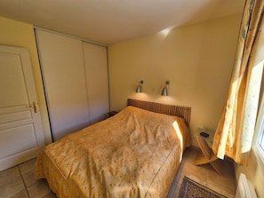 A bedroom with a bed, a nightstand, a lamp, and a window with curtains. - 3 rooms, in the heart of Saint Mandrier village (ST MANDRIER SUR MER)