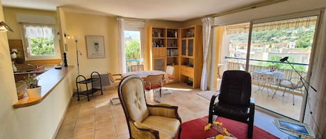 Un salon comprenant un coin repas, une bibliothèque et donnant sur un balcon aménagé avec du mobilier d’extérieur.
