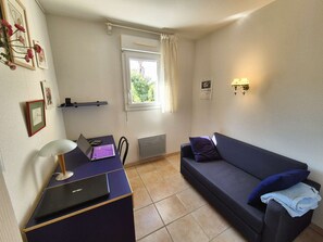 A small, furnished room with a desk, a couch, a radiator, a window with curtains, and wall-mounted lights. - 3 rooms, in the heart of Saint Mandrier village (ST MANDRIER SUR MER)