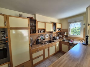 A kitchen with wooden cabinets, a stainless steel sink, and a window with a view of greenery. - 3 rooms, in the heart of Saint Mandrier village (ST MANDRIER SUR MER)