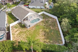 Vista aérea de una zona residencial con un amplio espacio exterior cerrado, posiblemente una piscina, rodeado de casas y vegetación.
