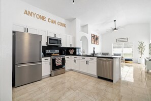 Cocina moderna con electrodomésticos de acero inoxidable, muebles blancos y una pared destacada con texto motivacional.