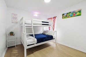 Una cama litera con escalera, una mesita de noche con una planta, y una pared con un cartel y un cuadro.