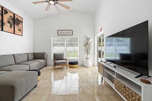 A modern living room with a grey sofa, a wooden chair, a potted plant, a flat-screen TV, and a ceiling fan. - Spacious 4-bedroom house in lovely Davenport with AC (Davenport)