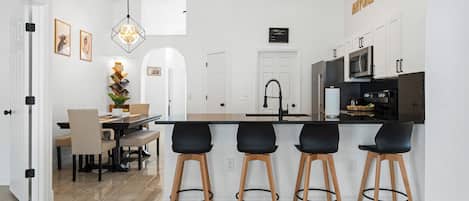 Une cuisine moderne avec un coin bar, des meubles blancs et un espace repas comprenant une table et des chaises.