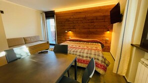 A room with a bed, a sofa, a table, and a TV mounted on the wall. - Villa Linda Bilo 1-4 Pax (Bardonecchia)