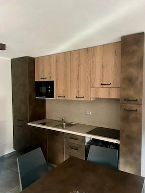 A compact kitchen with wooden cabinets, a built-in microwave, and a small dining area with chairs. - Villa Linda Bilo 1-4 Pax (Bardonecchia)