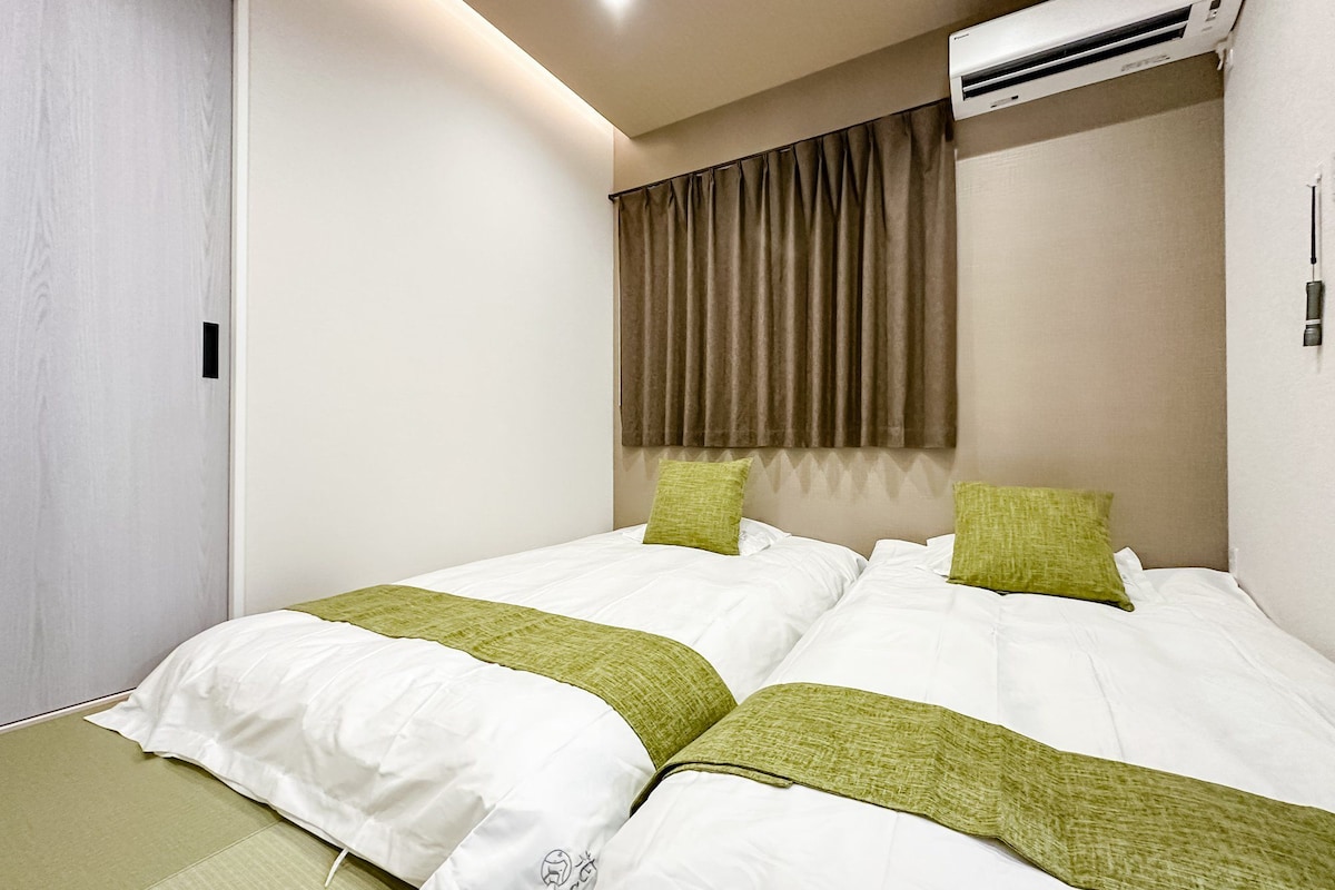 Ein Hotelzimmer mit zwei Betten, einem Vorhangfenster, einer Klimaanlage und einer Tür.
