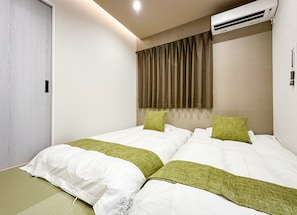 Ein Hotelzimmer mit zwei Betten, einem Vorhangfenster, einer Klimaanlage und einer Tür.