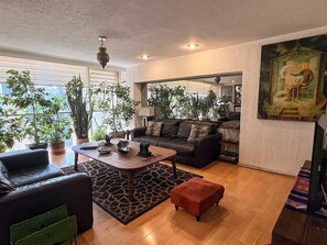 En moderne stue med sofa, sofabord og skammel. Der er plantede planter og et billede på væggen.
