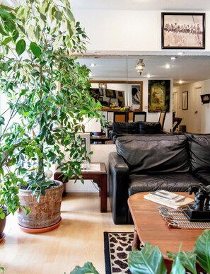 A living room with a black leather sofa, a coffee table with books and a horse figurine, a large potted plant, and a dining area in the background. - Polanco Connected | South, North & Mexico City (Mexico City)