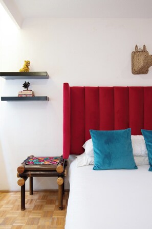 A bedroom with a red upholstered headboard, a wooden bedside table with a colorful blanket, and a bed with white and blue pillows. - Polanco Connected | South, North & Mexico City (Mexico City)
