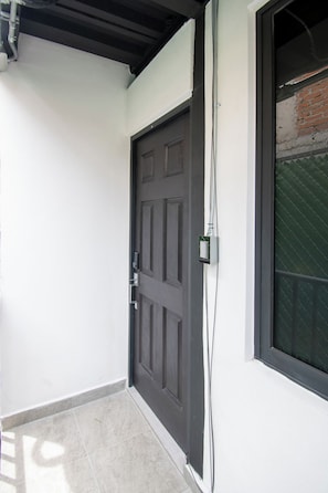 A closed dark-colored door with a modern handle, a window with a metal grid, and a white wall with a visible electrical conduit. - Modern Loft · 10 Min from Coyoacán Center (Mexico City)