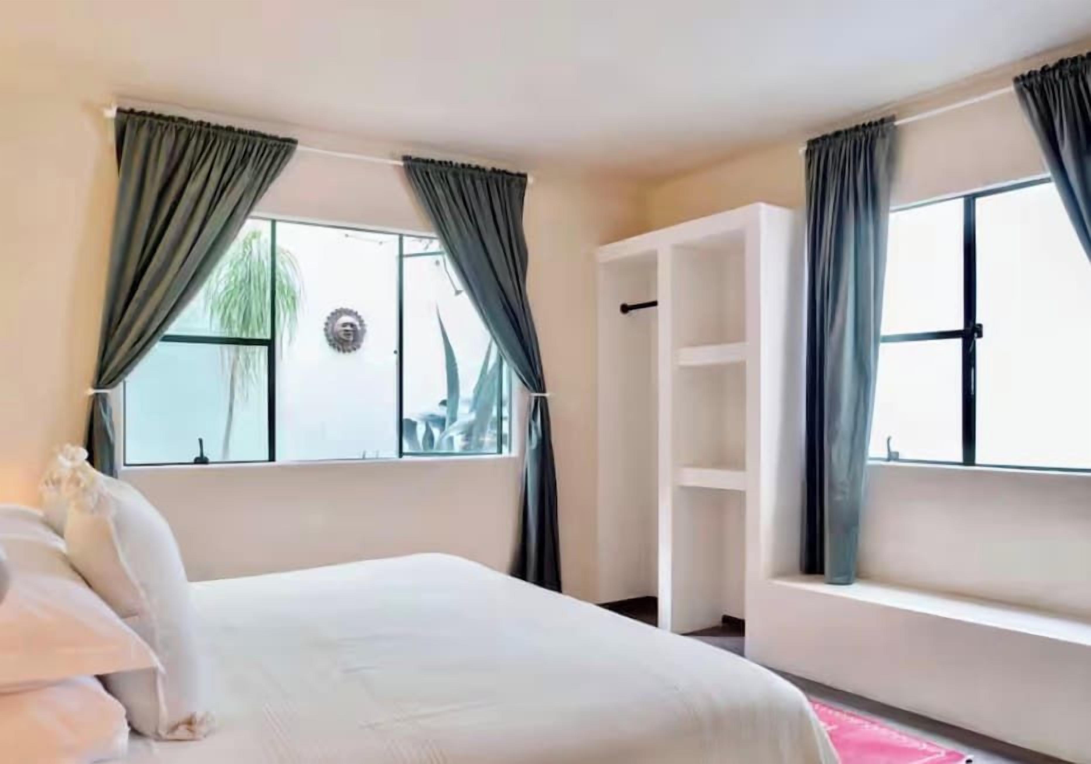 Quarto de hotel com cama, janela com cortinas, prateleira embutida branca e vista para o exterior.