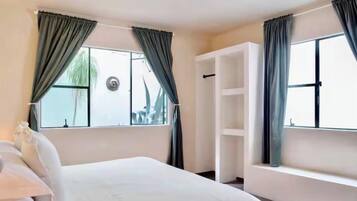 Quarto de hotel com cama, janela com cortinas, prateleira embutida branca e vista para o exterior.