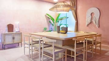 A dining area with a wooden table and chairs, a hanging lamp, and a macrame wall decoration.