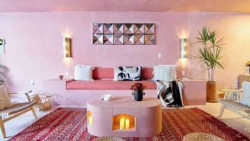 Ein gemütliches Wohnzimmer mit einem rosafarbenen Sofa, einem runden Couchtisch mit Kerzen und einem geometrischen Wandbild.